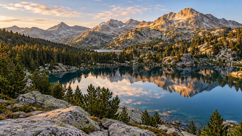 Un lac de montagne bordé de pins à crochets au pied du massif granitique du Néouvielle, par temps clair